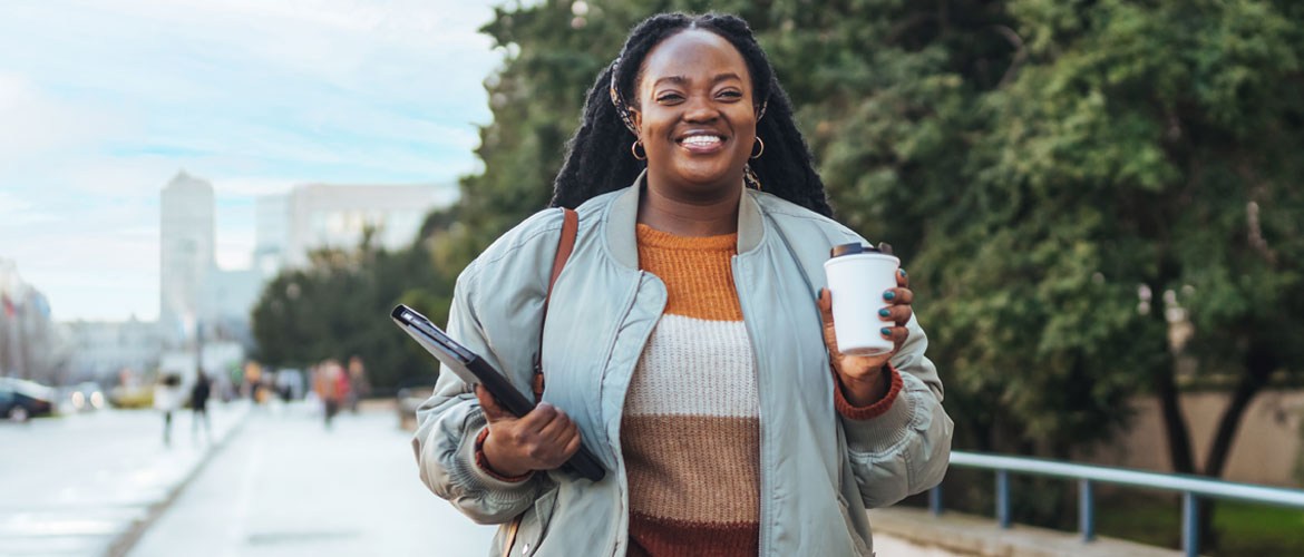 a woman smiling walking outside holding a travel mug